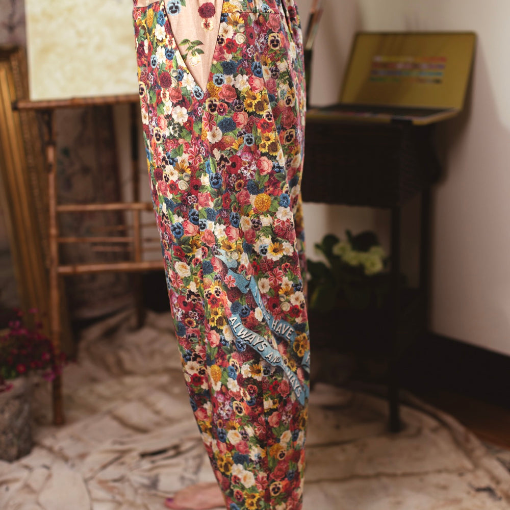 
                  
                    Artist pants featuring a whimsical print of 50 antique seed catalogue flowers arranged on a painter’s palette with a Monet quote – Market of Stars.
                  
                