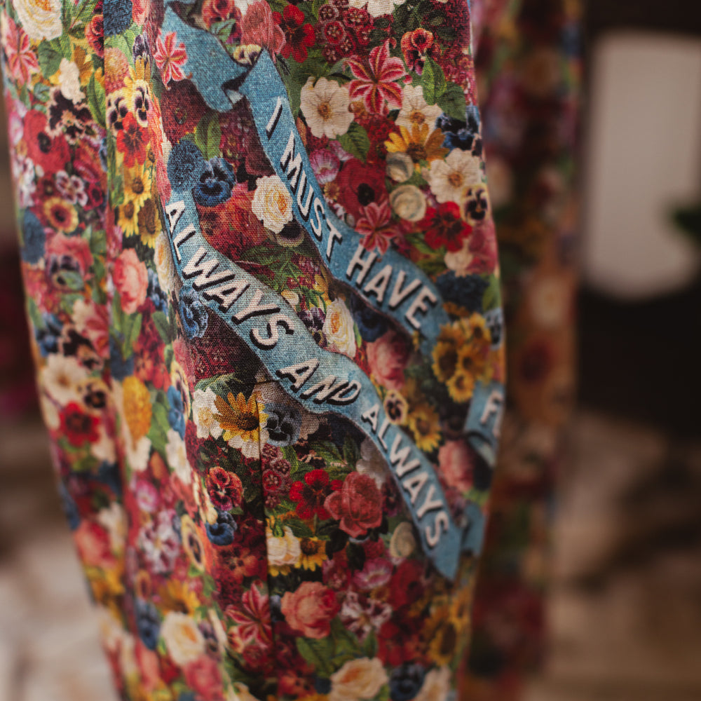 
                  
                    Artist pants featuring a whimsical print of 50 antique seed catalogue flowers arranged on a painter’s palette with a Monet quote – Market of Stars.
                  
                