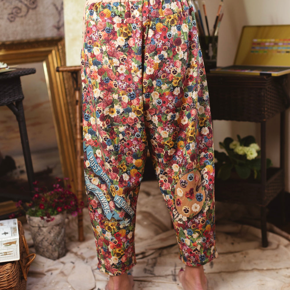 
                  
                    Artist pants featuring a whimsical print of 50 antique seed catalogue flowers arranged on a painter’s palette with a Monet quote – Market of Stars.
                  
                