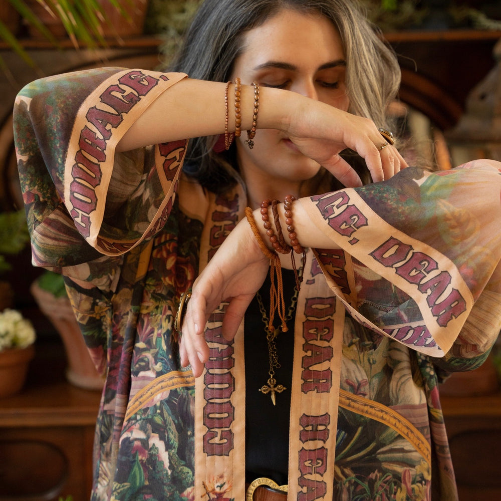 
                  
                    Model wearing Courage Dear Heart Pixie cut Duster featuring Victorian Sacred Heart art and hidden affirmations of courage and love on bamboo-based viscose – Market of Stars.
                  
                