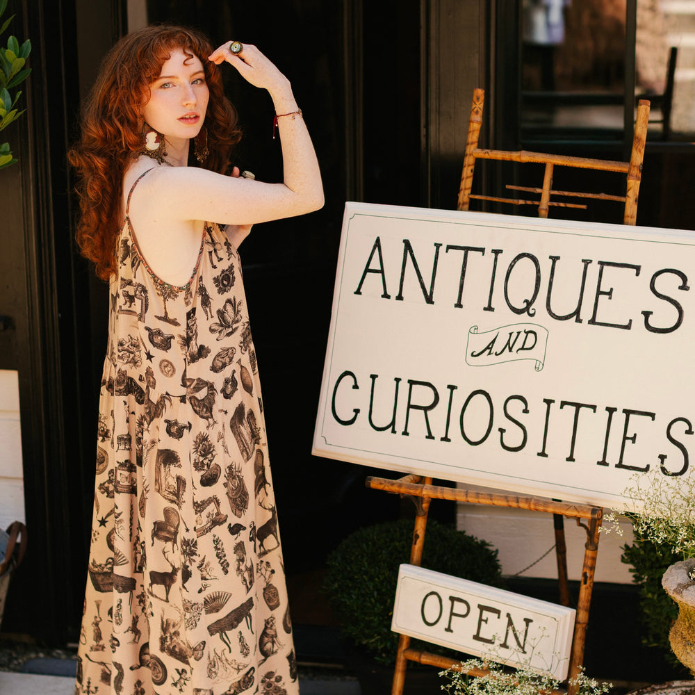 Model wearing a maxi-length bamboo viscose slip dress inspired by a mysterious Victorian scrapbook. This whimsical print celebrates the wonder hidden in ordinary things — Market of Stars.