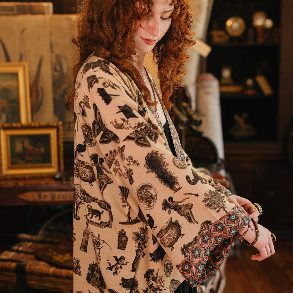 
                  
                    Model wearing a bamboo-viscose cropped length duster inspired by a mysterious Victorian scrapbook. This whimsical print celebrates the wonder hidden in ordinary things — Market of Stars.
                  
                