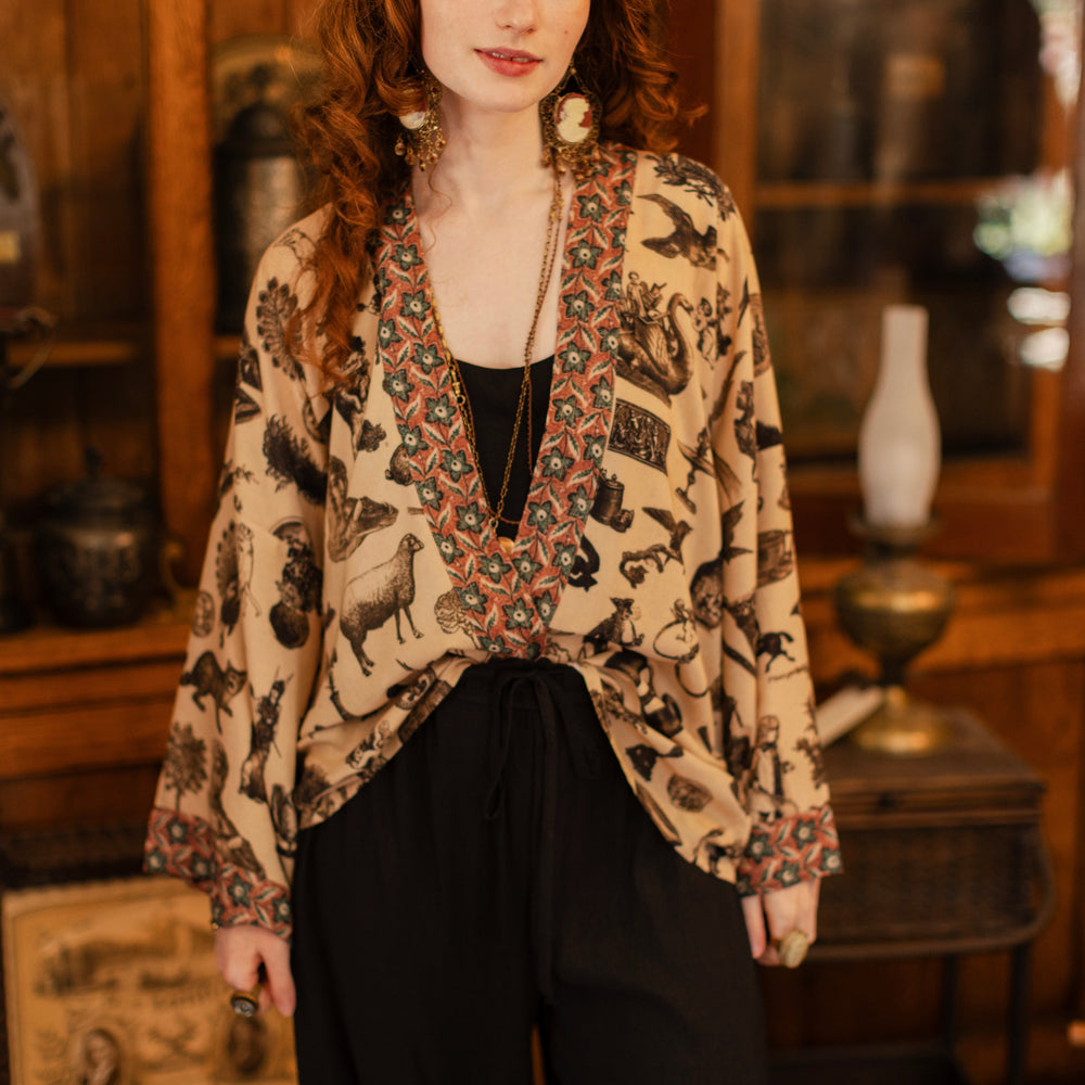 
                  
                    Model wearing a bamboo-viscose cropped length duster inspired by a mysterious Victorian scrapbook. This whimsical print celebrates the wonder hidden in ordinary things — Market of Stars.
                  
                