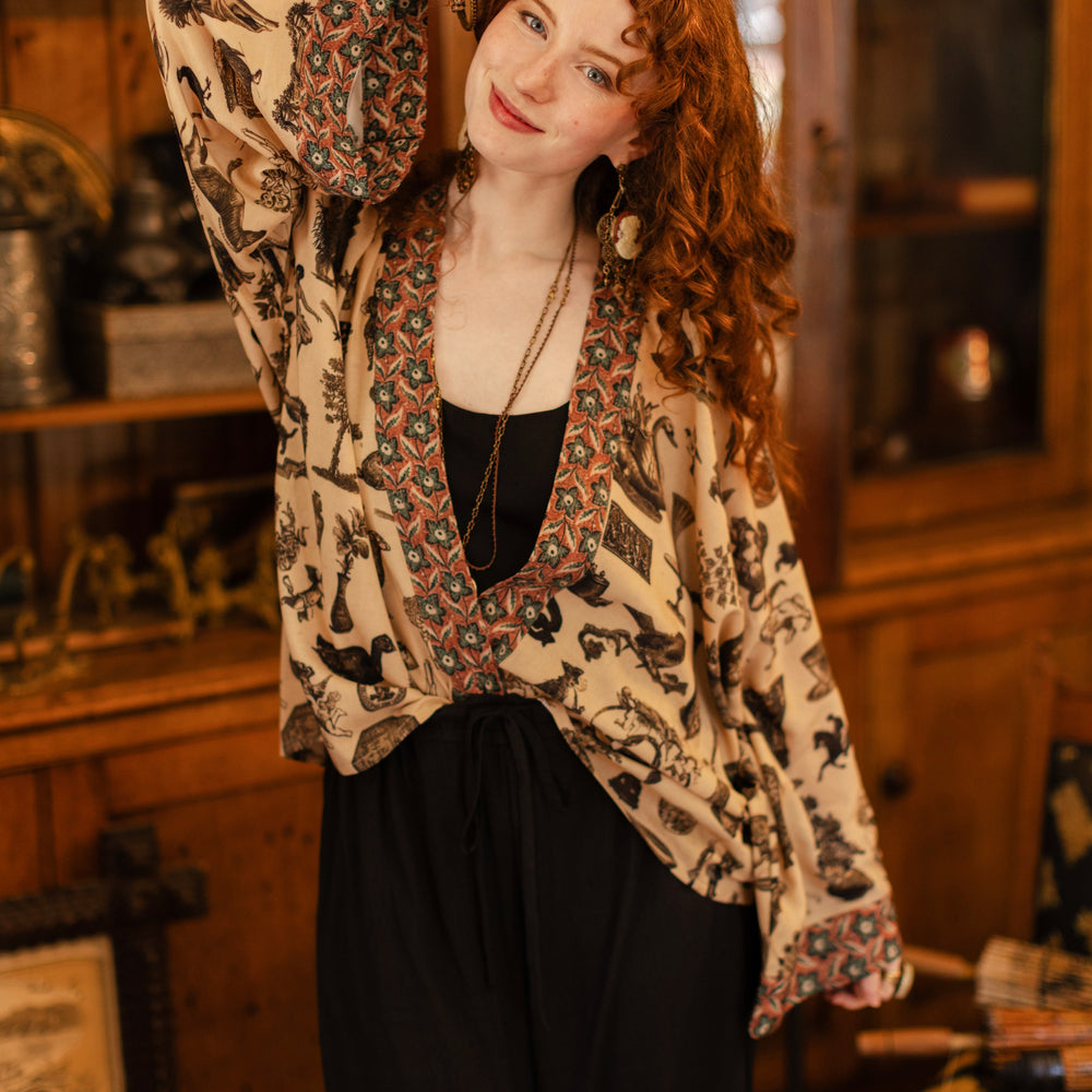 
                  
                    Model wearing a bamboo-viscose cropped length duster inspired by a mysterious Victorian scrapbook. This whimsical print celebrates the wonder hidden in ordinary things — Market of Stars.
                  
                