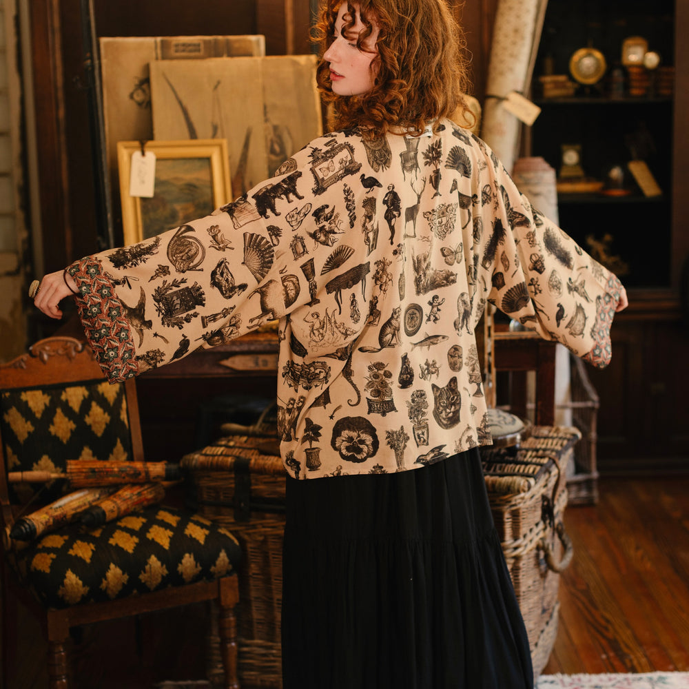 
                  
                    Model wearing a bamboo-viscose cropped length duster inspired by a mysterious Victorian scrapbook. This whimsical print celebrates the wonder hidden in ordinary things — Market of Stars.
                  
                