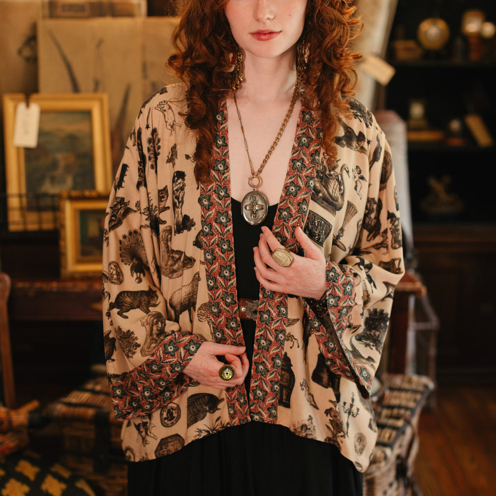 
                  
                    Model wearing a bamboo-viscose cropped length duster inspired by a mysterious Victorian scrapbook. This whimsical print celebrates the wonder hidden in ordinary things — Market of Stars.
                  
                