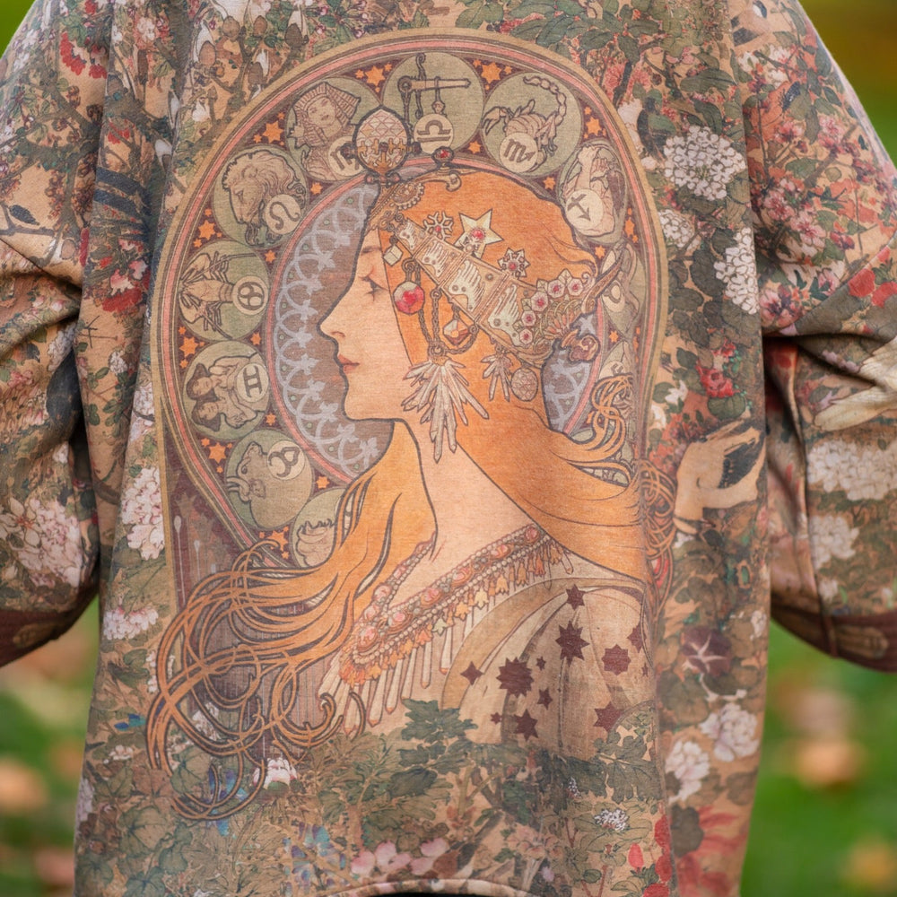 
                  
                    Model wearing Dreamweaver Cottage Cardigan featuring Mucha’s 1896 zodiac woman with celestial crown, printed on cozy fleece-lined cotton blend – Market of Stars
                  
                