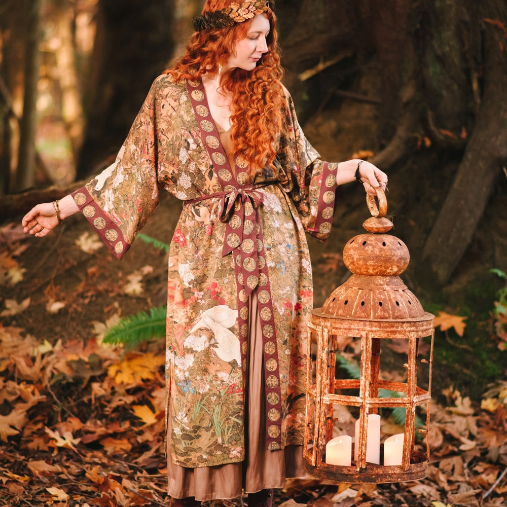 
                  
                    Model wearing Dreamweaver Opera Duster – featuring Alphonse Mucha’s zodiac woman, celestial crown, and burgundy zodiac trim inspired by 1970s luxe bohemian style – Market of Stars.
                  
                