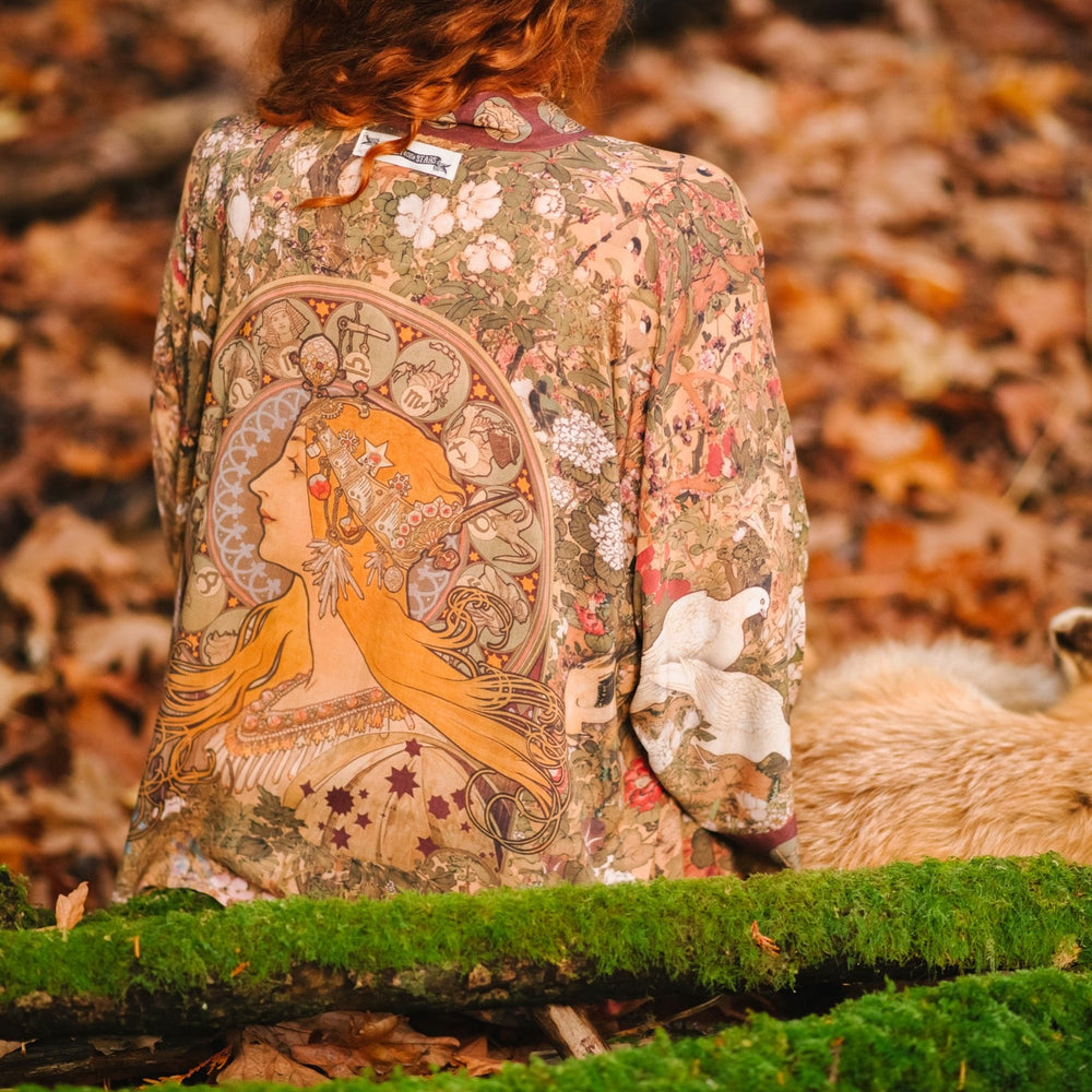 
                  
                    Model wearing Dreamweaver Matinée Duster featuring Alphonse Mucha’s 1896 zodiac woman – trimmed with celestial symbols on deep burgundy background – Market of Stars.
                  
                