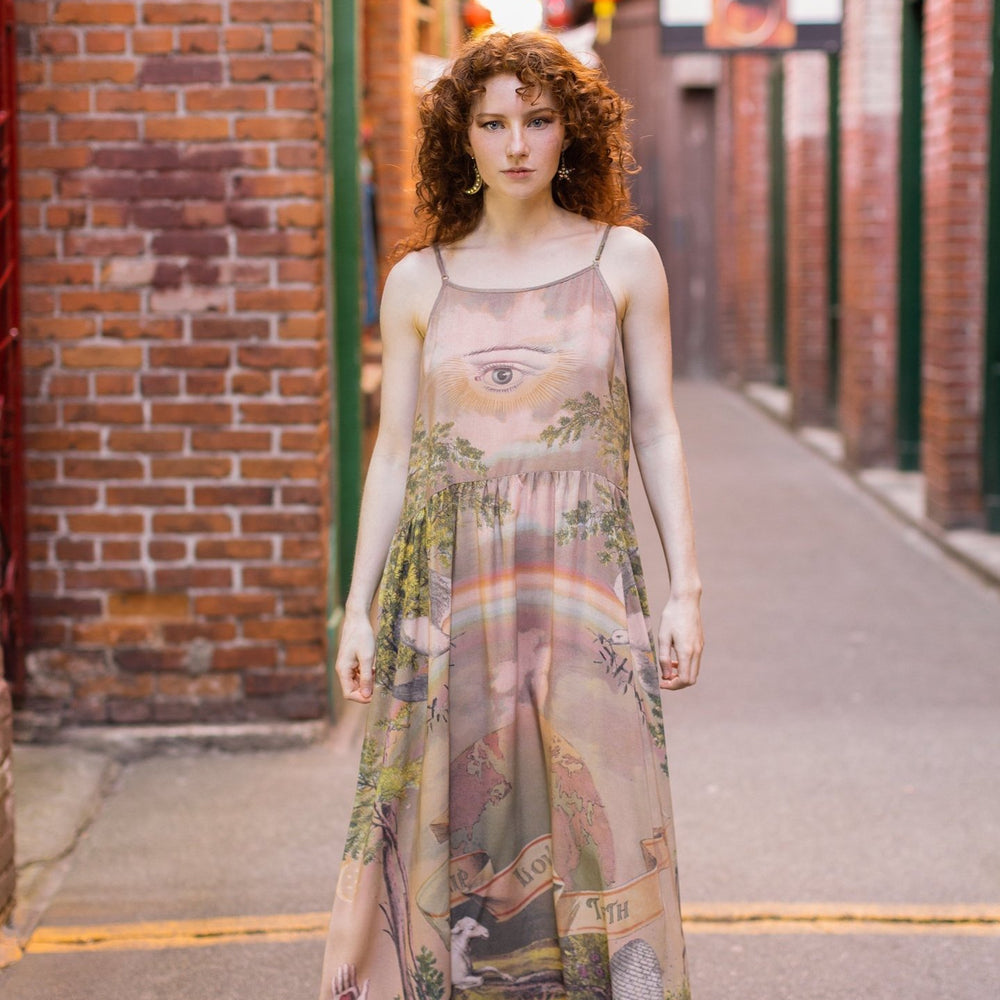 
                  
                    Model wearing sun-washed Bohéme slip dress featuring historic symbols of friendship, love, and truth in soft lavender, sage, gold, and aqua – Market of Stars.
                  
                