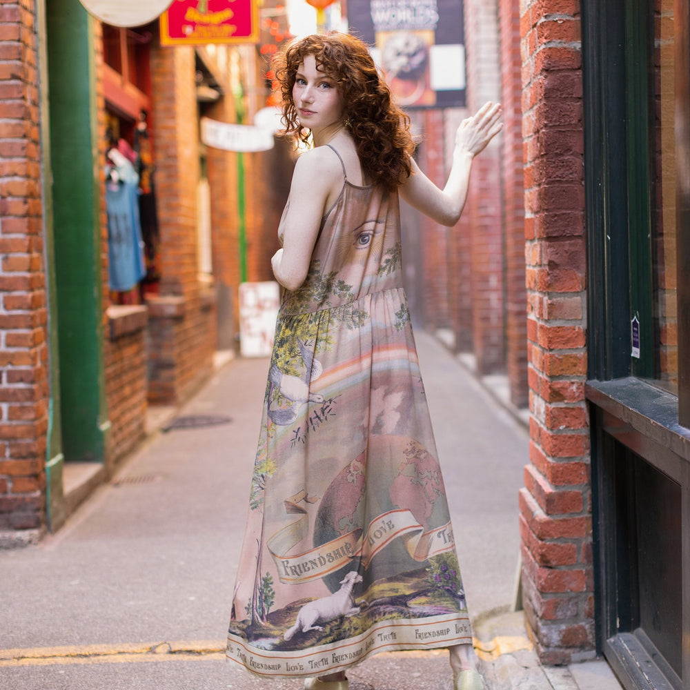 
                  
                    Model wearing sun-washed Bohéme slip dress featuring historic symbols of friendship, love, and truth in soft lavender, sage, gold, and aqua – Market of Stars.
                  
                