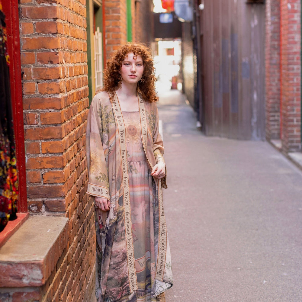 
                  
                    Model wearing sun-washed vintage-inspired Opera Duster featuring symbols of friendship, love, and truth in soft lavender, sage, gold, and aqua – Market of Stars
                  
                