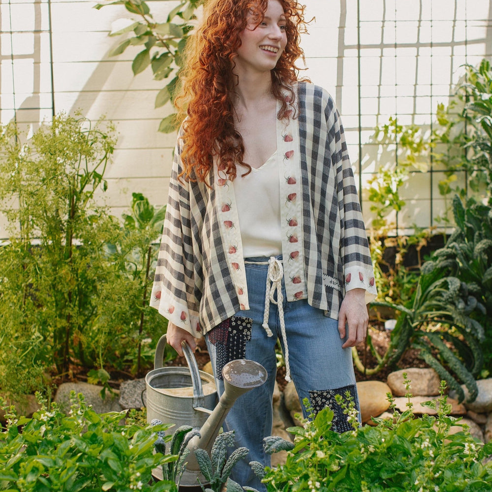 
                  
                    Model wearing Happy Days pixie cut kimono featuring heritage gingham, vintage strawberries, and a cross-stitch patch inspired by an 1836 sampler – Market of Stars.
                  
                