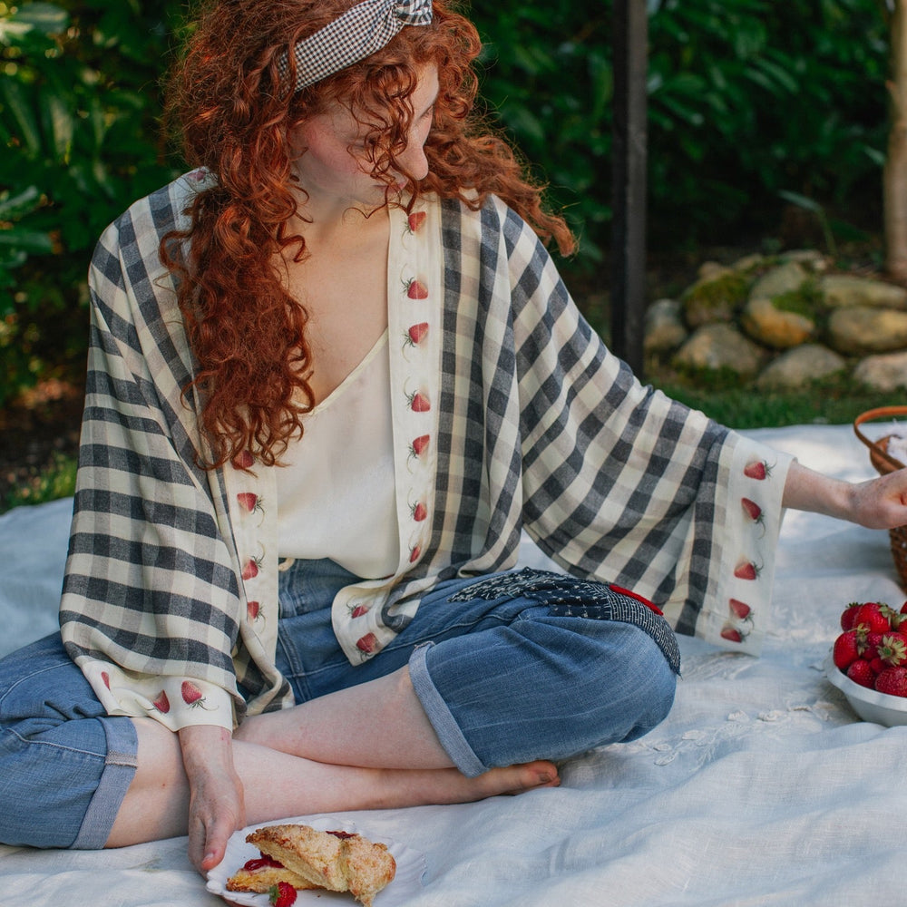 
                  
                    Model wearing Happy Days pixie cut kimono featuring heritage gingham, vintage strawberries, and a cross-stitch patch inspired by an 1836 sampler – Market of Stars.
                  
                