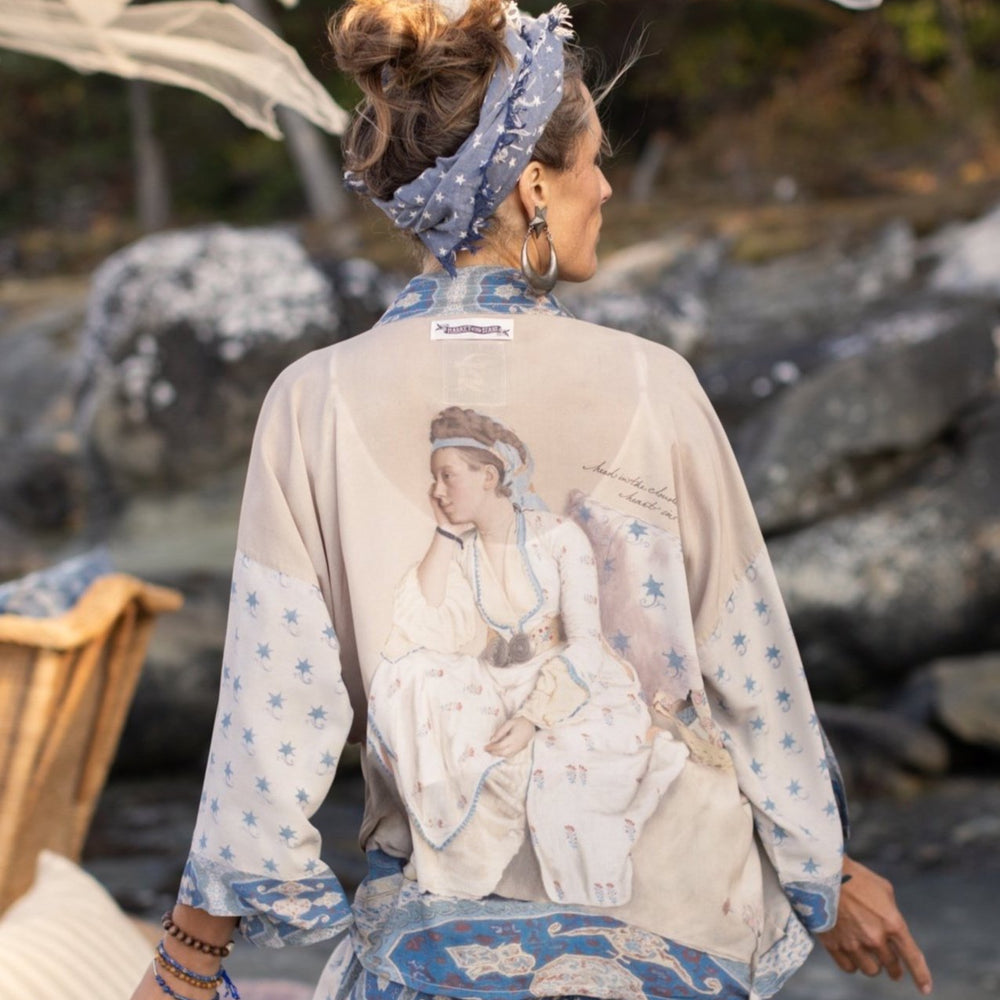 
                  
                    Model wearing the Head in the Clouds Opera Duster featuring Liotard’s portrait of his wife with Turkish textiles, starry sleeves, and poetic script – Market of Stars.
                  
                