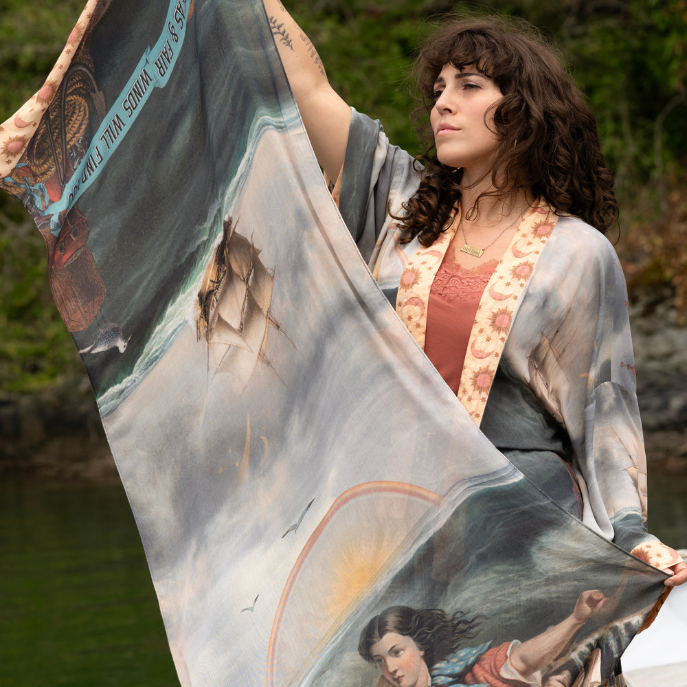 
                  
                    Model wearing the Hold Fast bamboo viscose scarf featuring a Victorian woman bravely rowing through a storm, seagulls, and rainbow horizon – Market of Stars.
                  
                