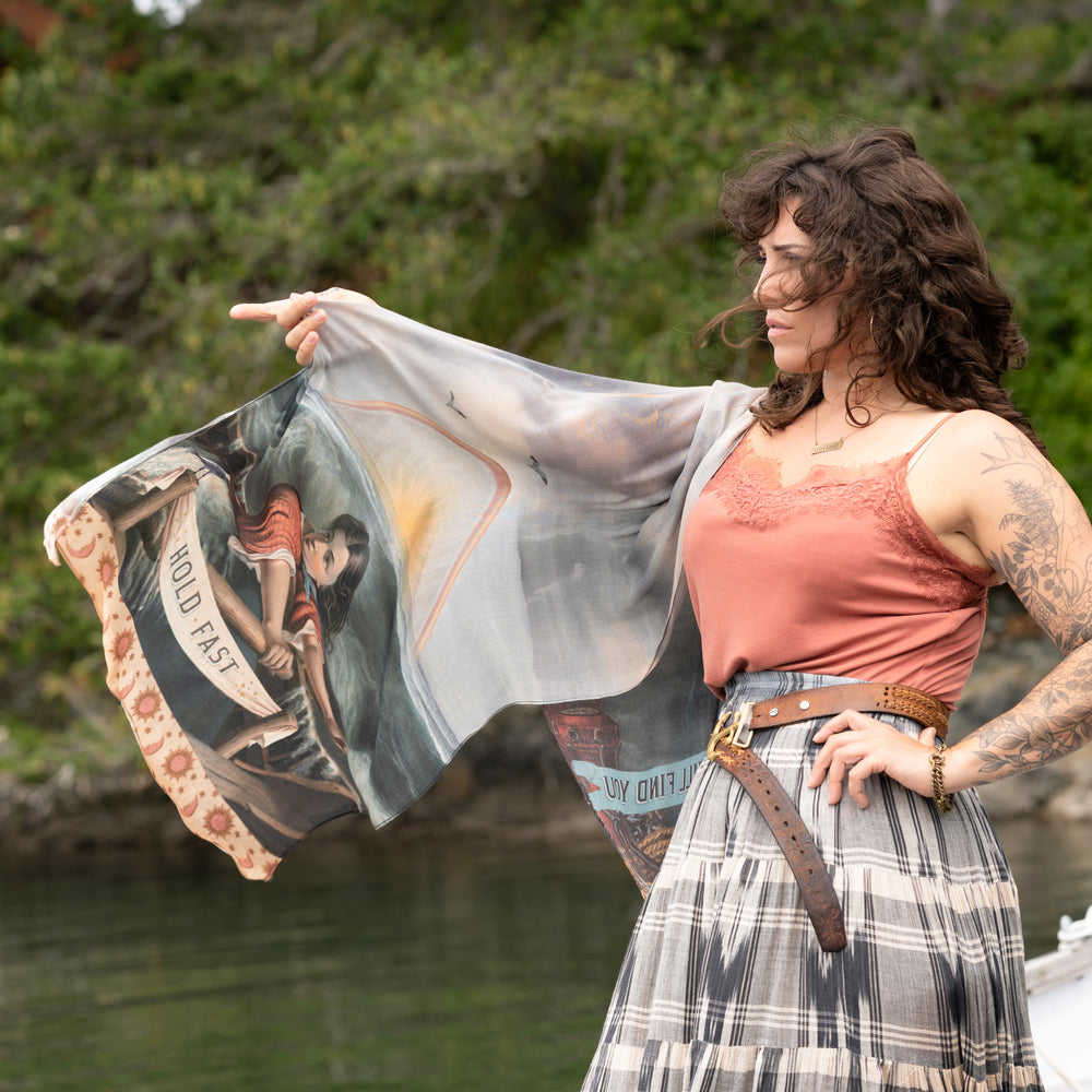
                  
                    Model wearing the Hold Fast bamboo viscose scarf featuring a Victorian woman bravely rowing through a storm, seagulls, and rainbow horizon – Market of Stars.
                  
                