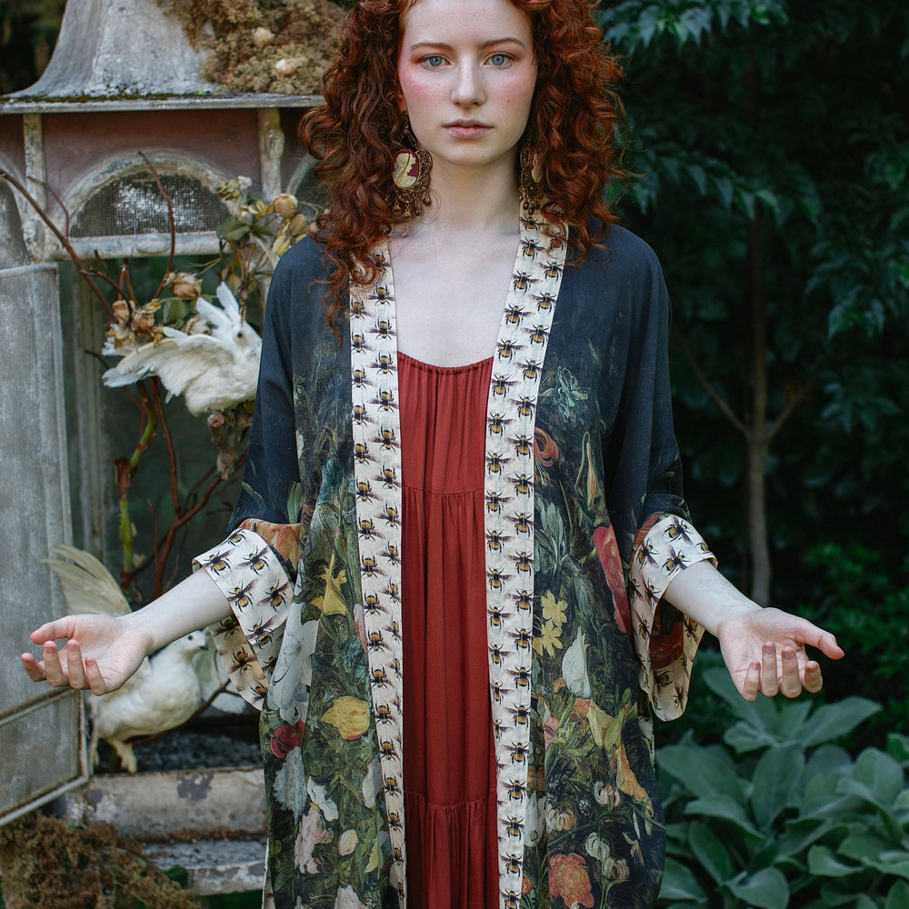 
                  
                    Model wearing the I Dream in Flowers Opera Duster featuring floral oil painting by Jan Brueghel and Victorian bumblebee trim – Market of Stars.
                  
                