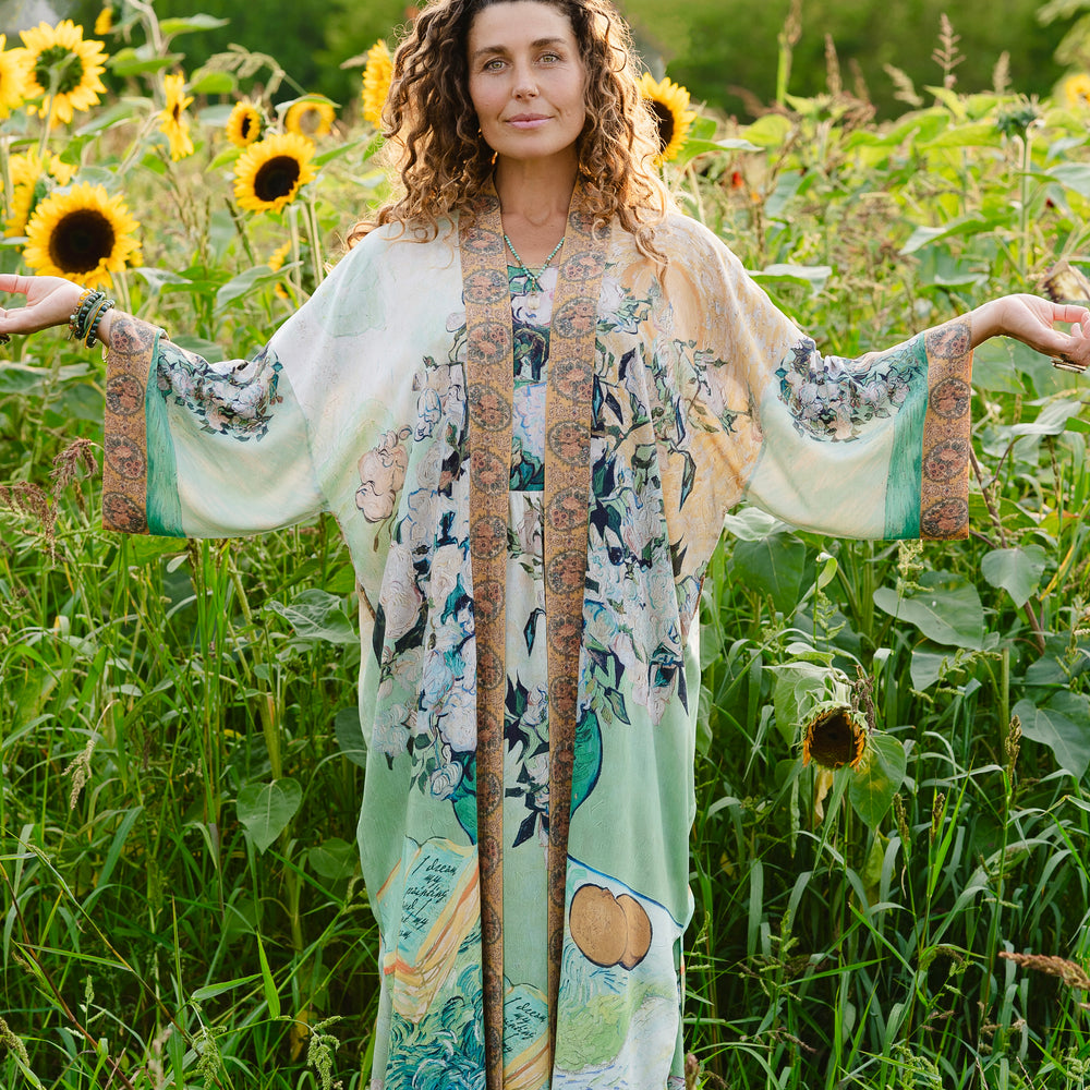 
                  
                    Model wearing long kimono duster featuring Van Gogh artwork and quote, with painted blossoms, book, sun, and eye in rich tones of jade and gold - Market of Stars
                  
                