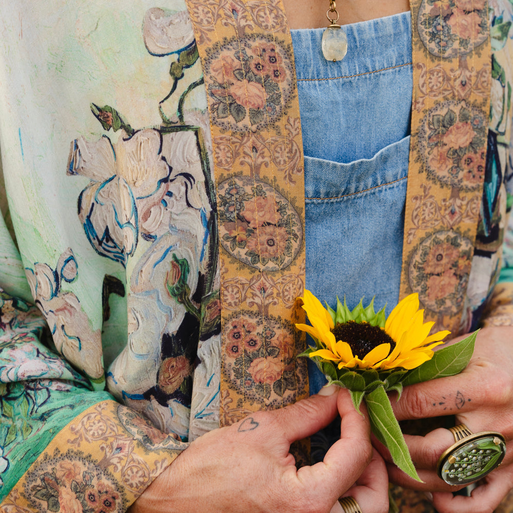 
                  
                    Model wearing long kimono duster featuring Van Gogh artwork and quote, with painted blossoms, book, sun, and eye in rich tones of jade and gold - Market of Stars
                  
                