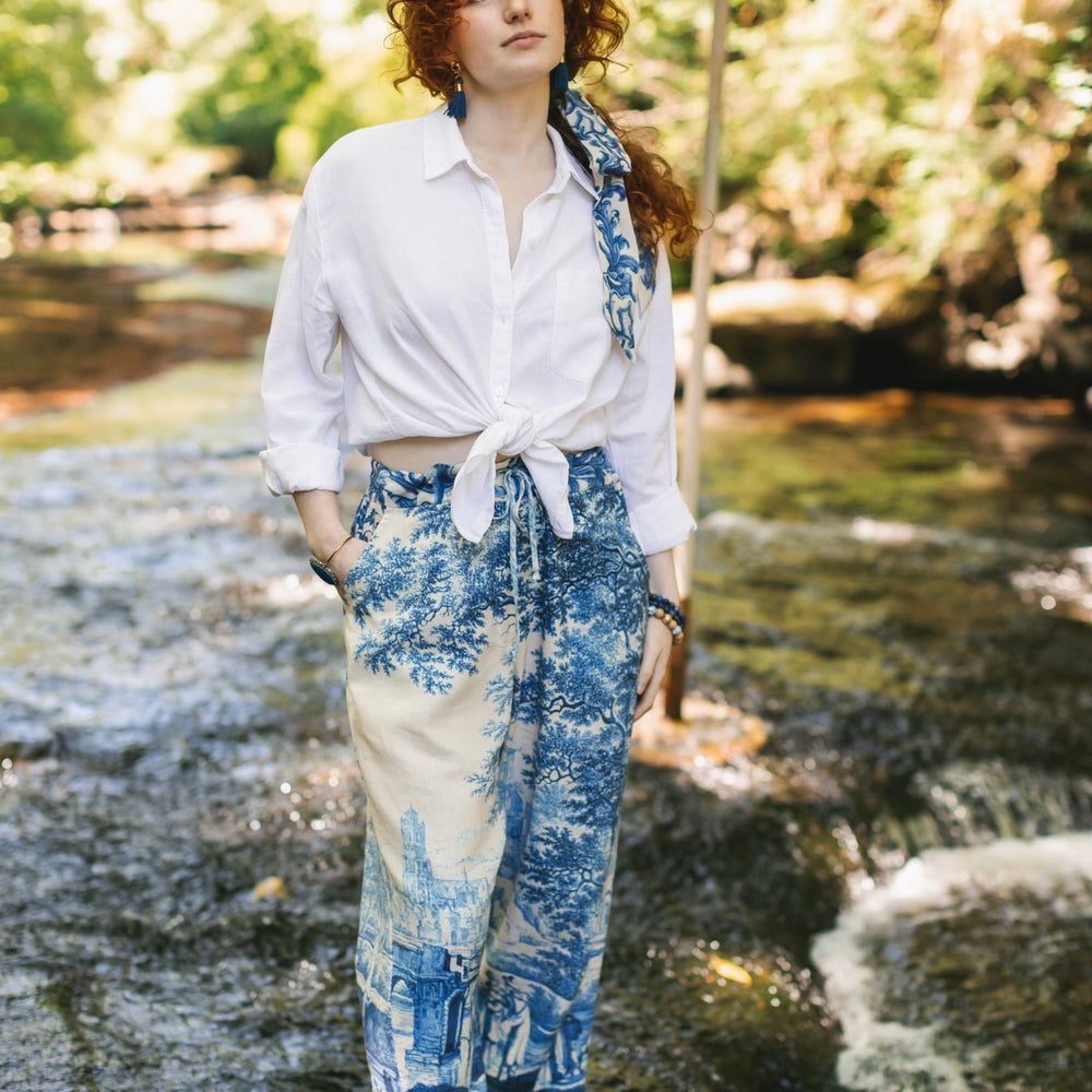 Model wearing Let the Light In linen Artist Pant featuring print of Delft blue and white landscape pottery, and positive message of light and hope - Market of Stars