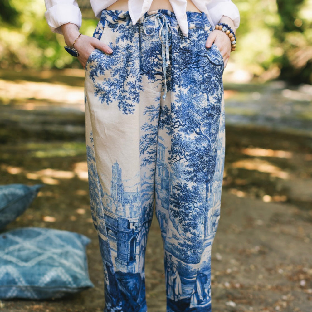 Model wearing Let the Light In linen Artist Pant featuring print of Delft blue and white landscape pottery, and positive message of light and hope - Market of Stars