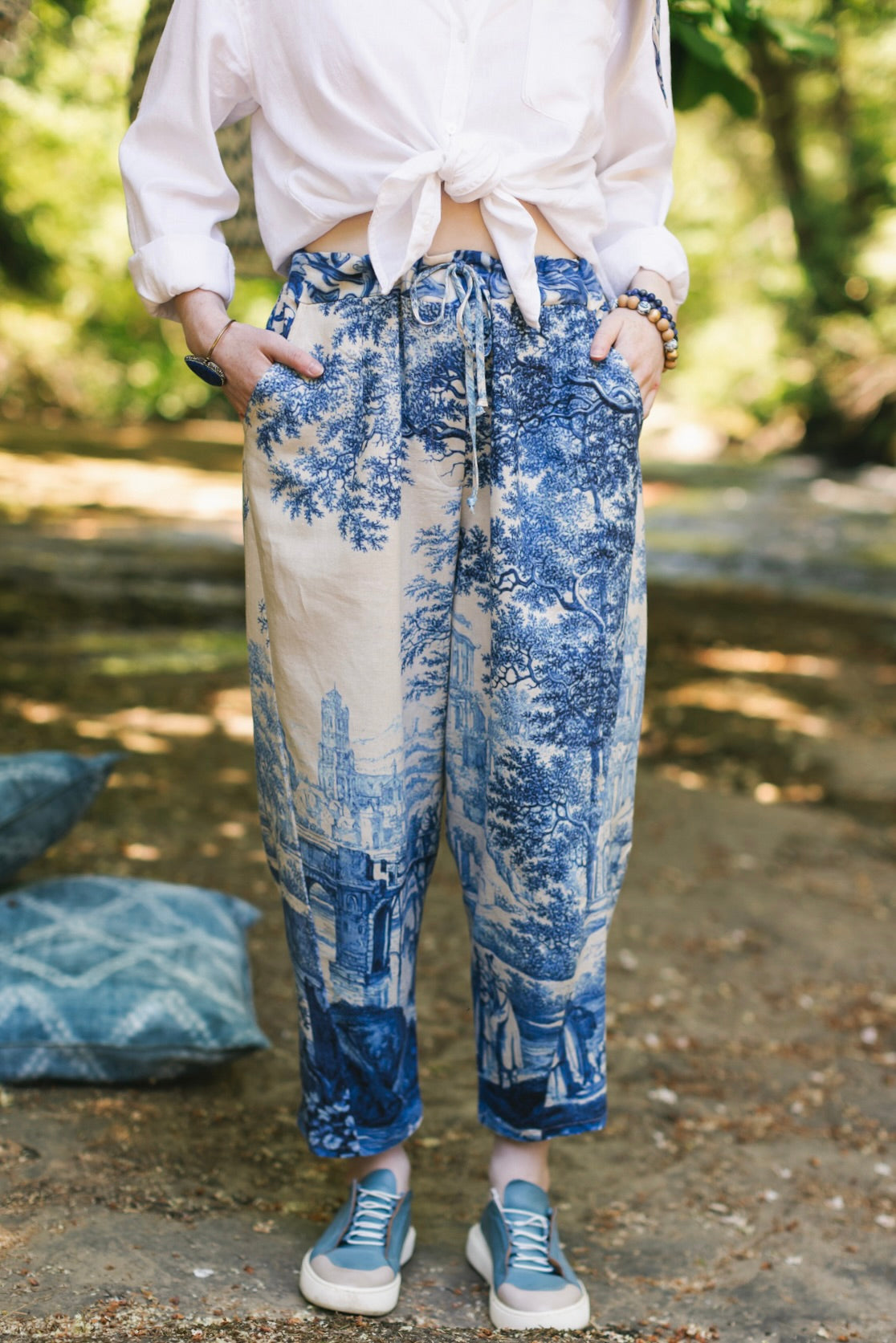 Model wearing Let the Light In linen Artist Pant featuring print of Delft blue and white landscape pottery, and positive message of light and hope - Market of Stars