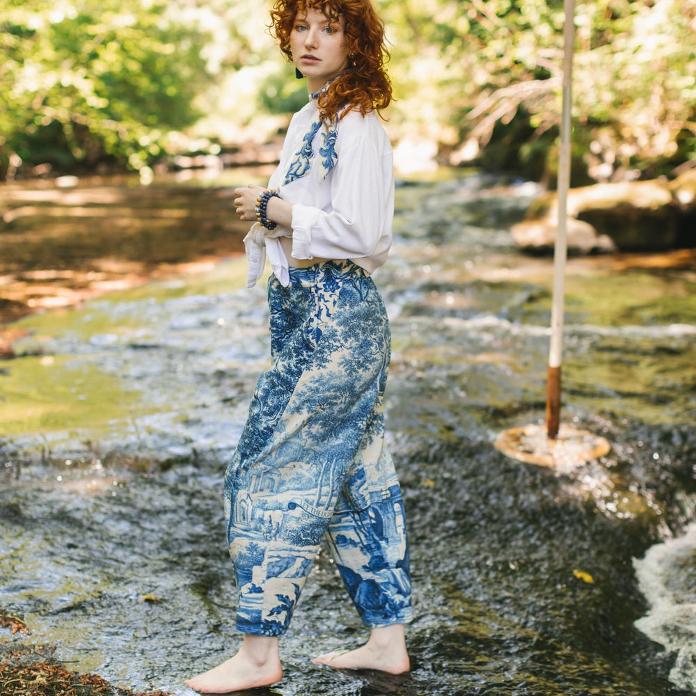 
                  
                    Model wearing Let the Light In linen Artist Pant featuring print of Delft blue and white landscape pottery, and positive message of light and hope - Market of Stars
                  
                