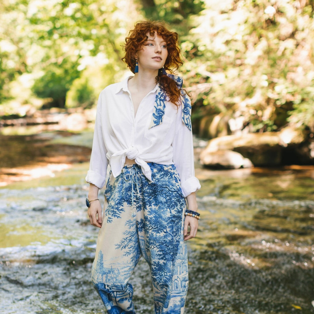 
                  
                    Model wearing Let the Light In linen Artist Pant featuring print of Delft blue and white landscape pottery, and positive message of light and hope - Market of Stars
                  
                