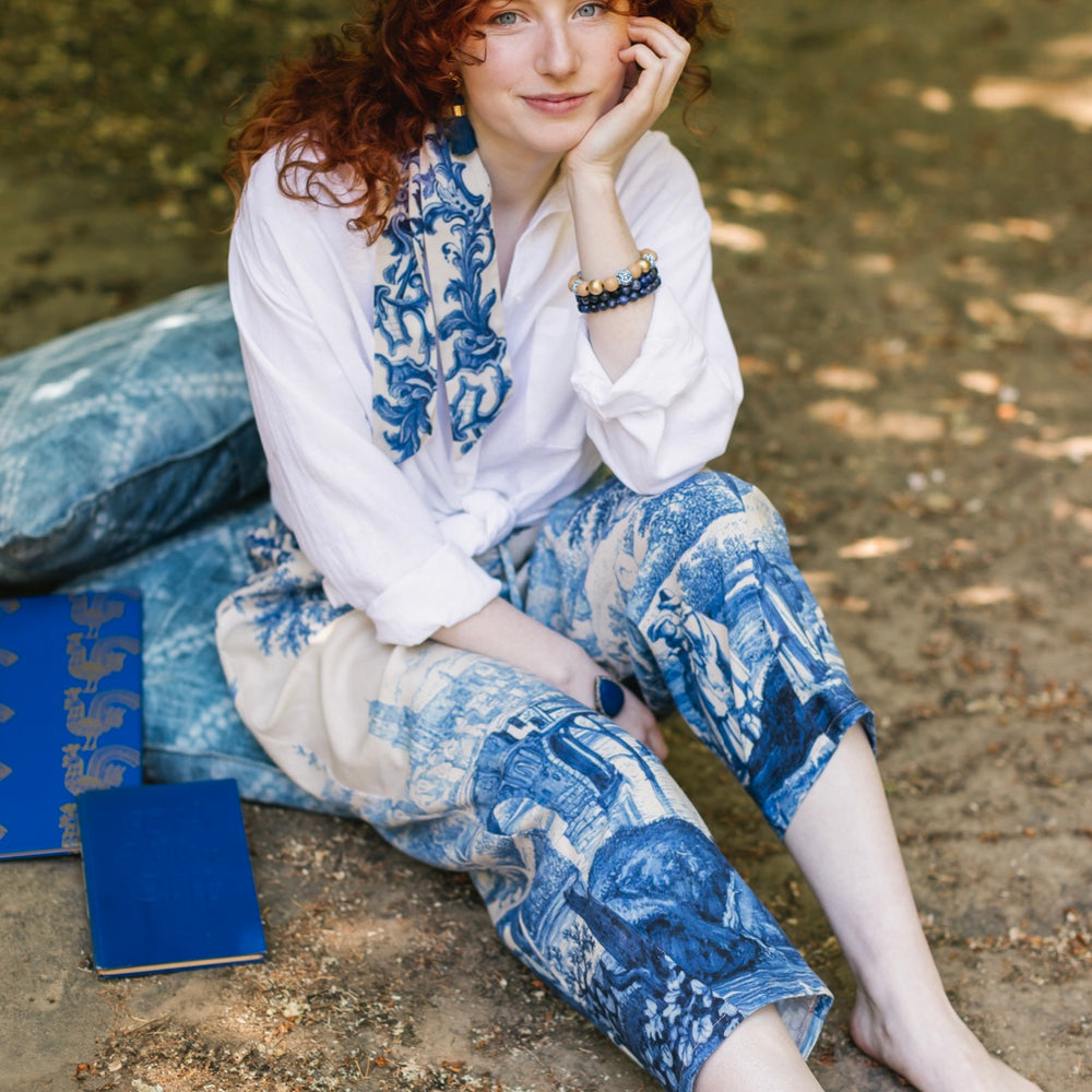 
                  
                    Model wearing Let the Light In linen Artist Pant featuring print of Delft blue and white landscape pottery, and positive message of light and hope - Market of Stars
                  
                