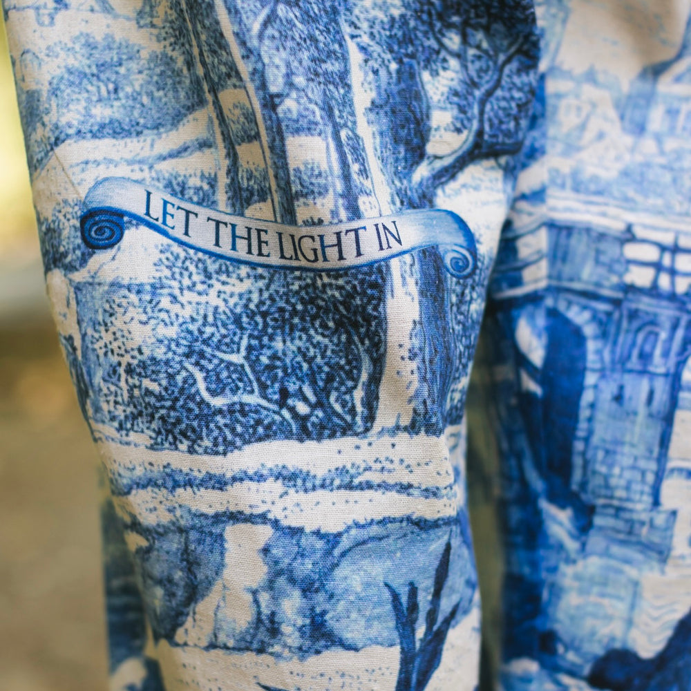 
                  
                    Model wearing Let the Light In linen Artist Pant featuring print of Delft blue and white landscape pottery, and positive message of light and hope - Market of Stars
                  
                