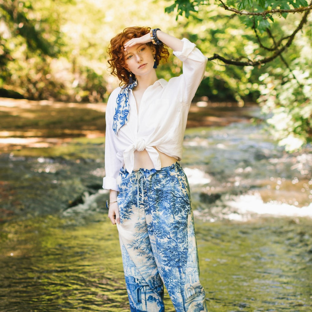 
                  
                    Model wearing Let the Light In linen Artist Pant featuring print of Delft blue and white landscape pottery, and positive message of light and hope - Market of Stars
                  
                