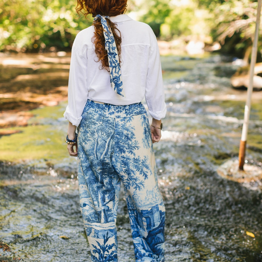 
                  
                    Model wearing Let the Light In linen Artist Pant featuring print of Delft blue and white landscape pottery, and positive message of light and hope - Market of Stars
                  
                