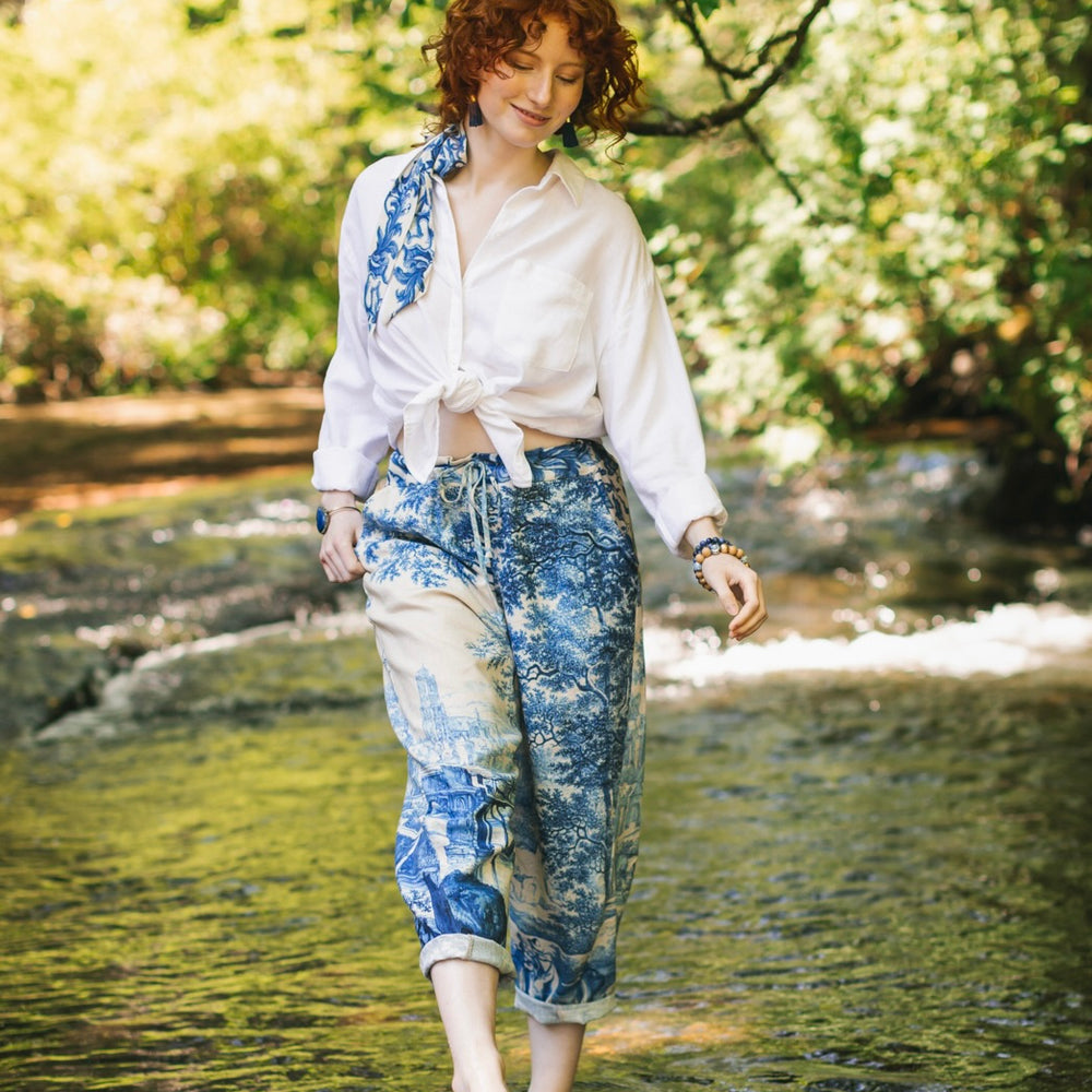 
                  
                    Model wearing Let the Light In linen Artist Pant featuring print of Delft blue and white landscape pottery, and positive message of light and hope - Market of Stars
                  
                