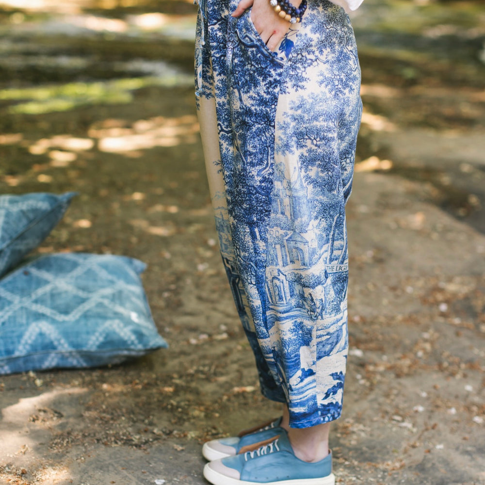 
                  
                    Model wearing Let the Light In linen Artist Pant featuring print of Delft blue and white landscape pottery, and positive message of light and hope - Market of Stars
                  
                
