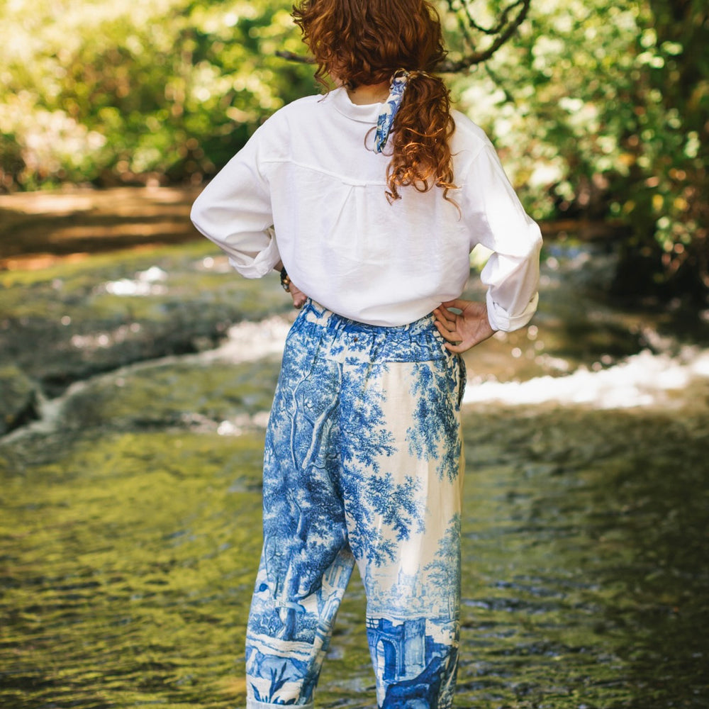 
                  
                    Model wearing Let the Light In linen Artist Pant featuring print of Delft blue and white landscape pottery, and positive message of light and hope - Market of Stars
                  
                
