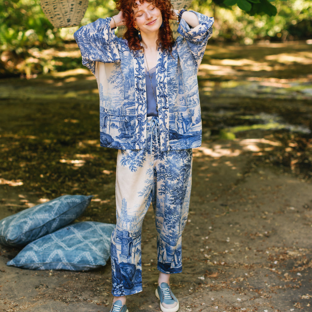 
                  
                    Model wearing Let the Light In linen Artist Pant featuring print of Delft blue and white landscape pottery, and positive message of light and hope - Market of Stars
                  
                