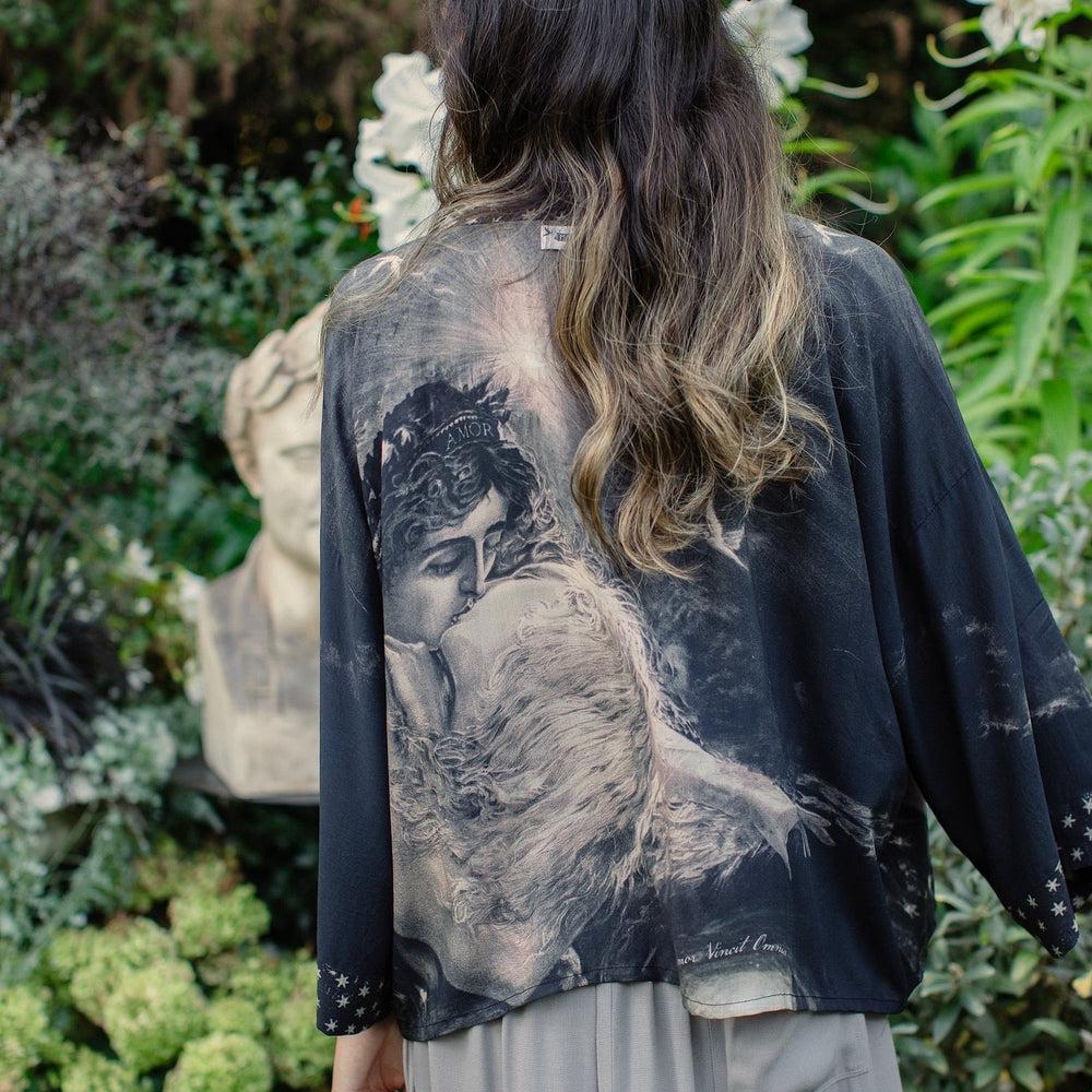 
                  
                    Model wearing Love Conquers All Kimono featuring an 1800s heart-shaped embrace, doves, crescent moon, and the words Amor Vincit Omnia – Market of Stars.
                  
                