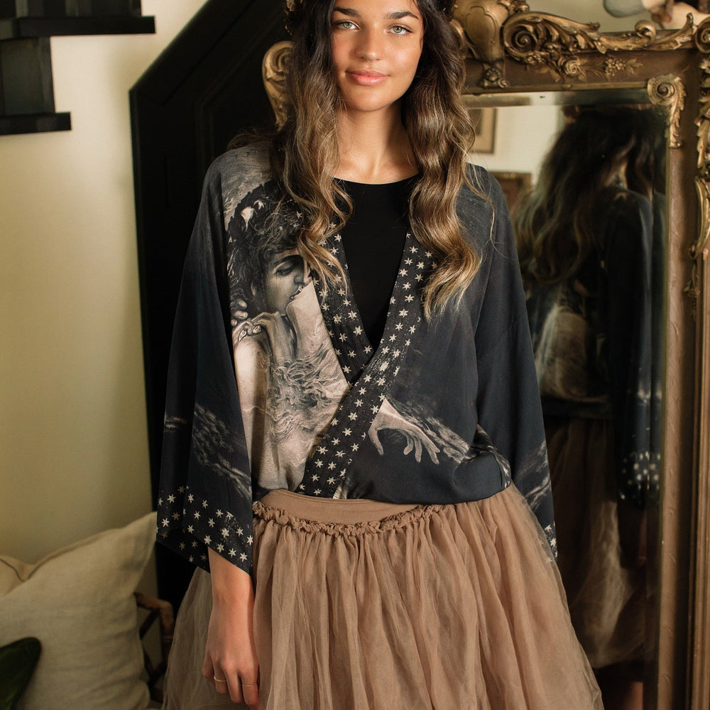 
                  
                    Model wearing Love Conquers All Kimono featuring an 1800s heart-shaped embrace, doves, crescent moon, and the words Amor Vincit Omnia – Market of Stars.
                  
                