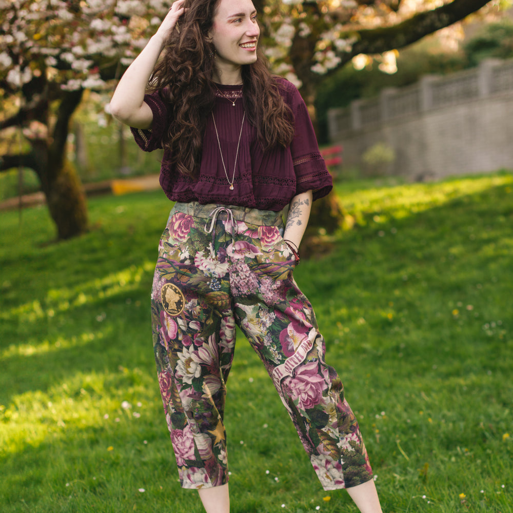 Model wearing linen blend artist pants featuring antique wishbone–Victorian coin–evening star–dandelion art and “Wish with Me” banner on floral background – Market of Stars