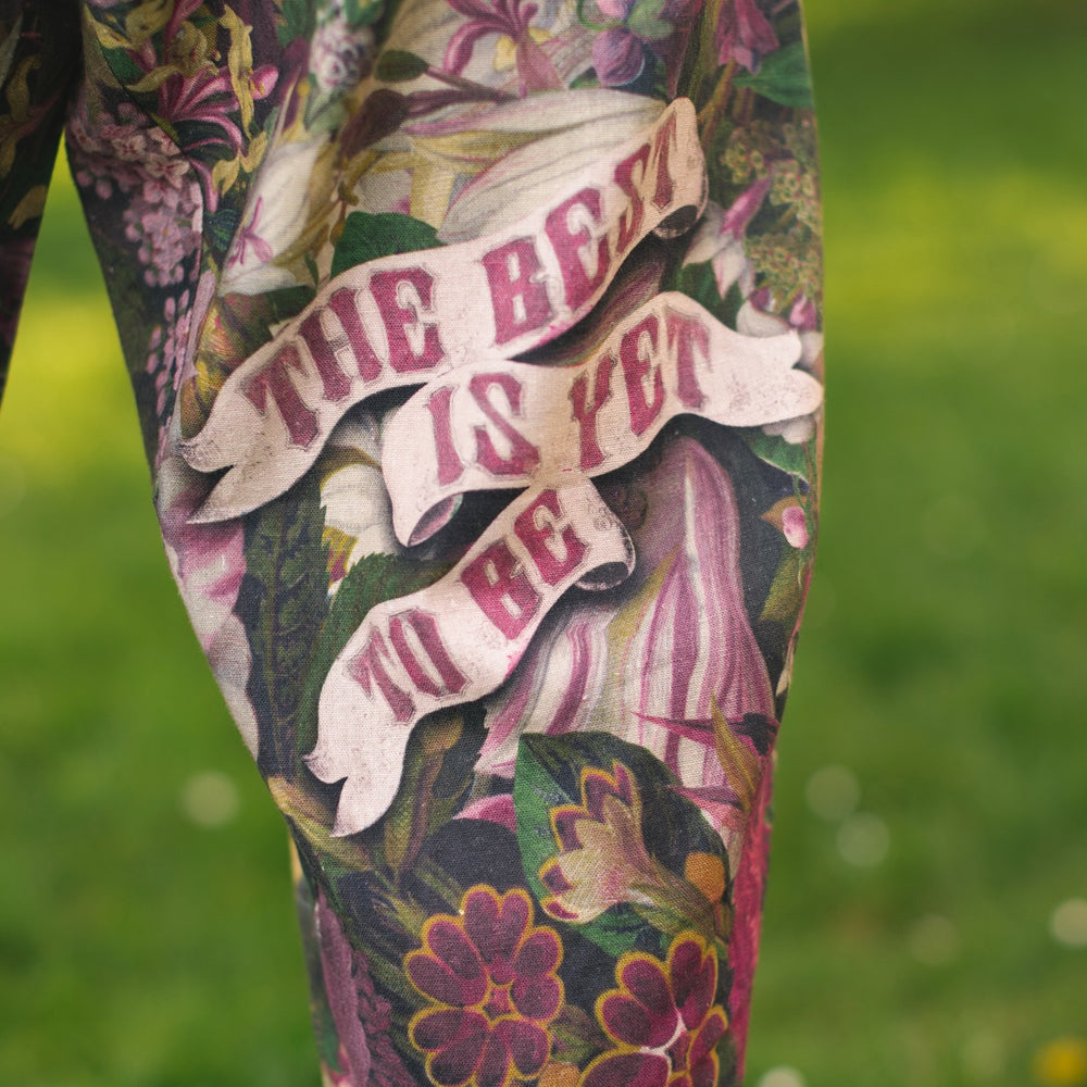 
                  
                    Model wearing linen blend artist pants featuring antique wishbone–Victorian coin–evening star–dandelion art and “Wish with Me” banner on floral background – Market of Stars
                  
                