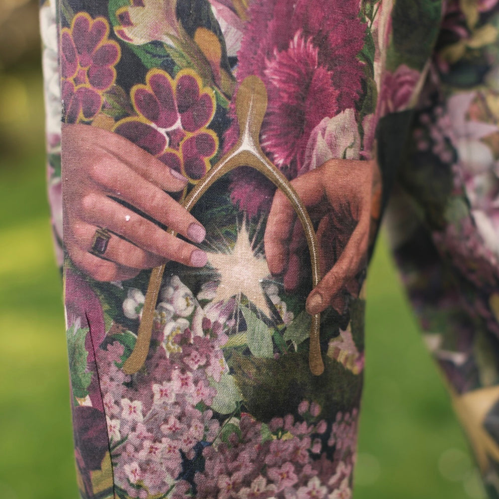 
                  
                    Model wearing linen blend artist pants featuring antique wishbone–Victorian coin–evening star–dandelion art and “Wish with Me” banner on floral background – Market of Stars
                  
                