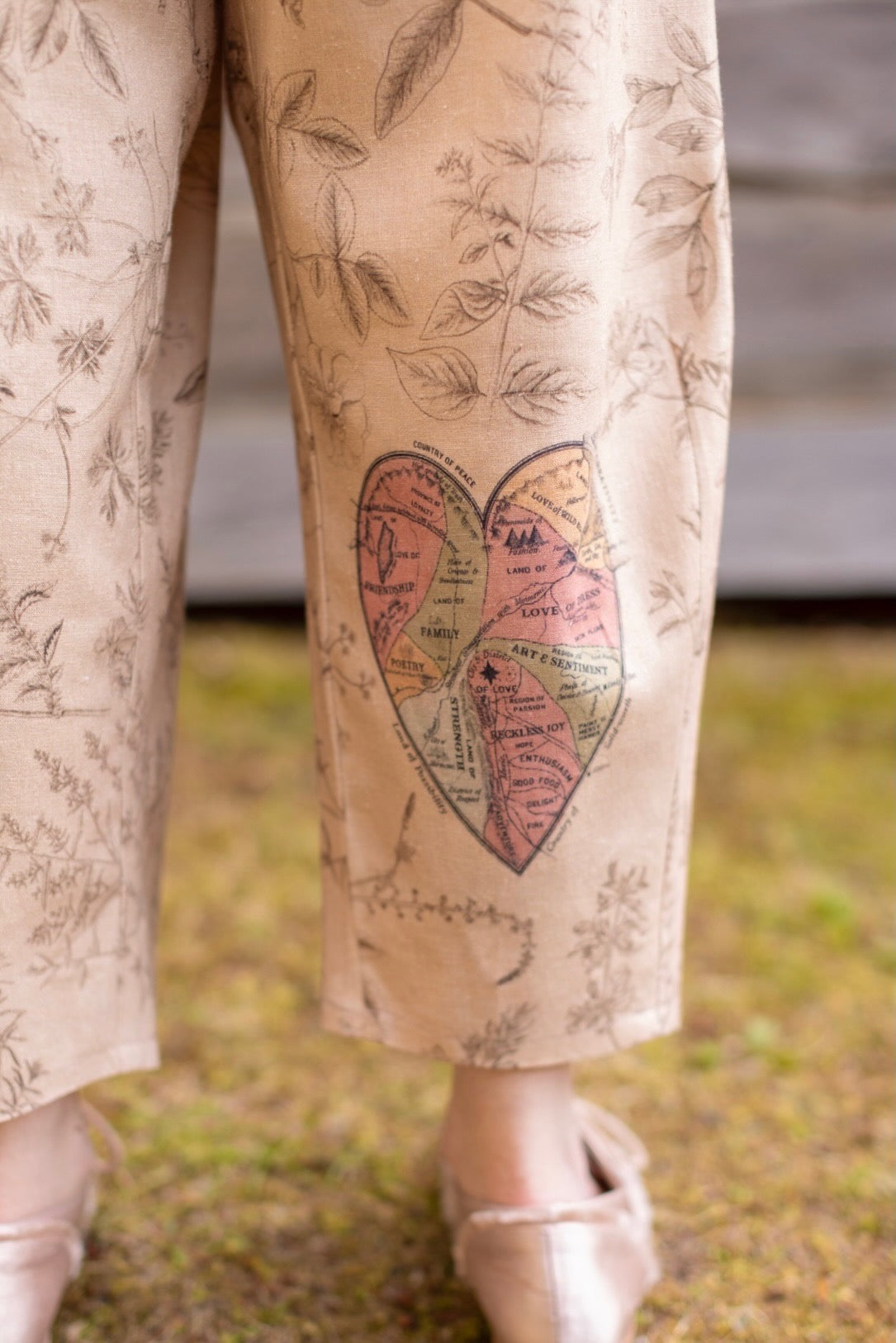Model wearing artist pants in oat featuring reimagined vintage 1846 map of a woman’s heart with playful updated place names – Market of Stars