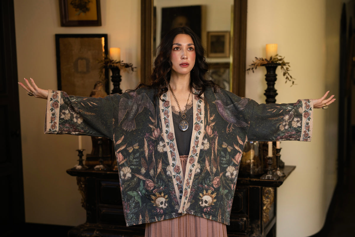 Model wearing a cozy fleece lined cottage cardigan ft. artwork created by Jessica Roux including two starlings beneath a full moon with flowers, butterflies, moths and botanical artwork - Market of Stars