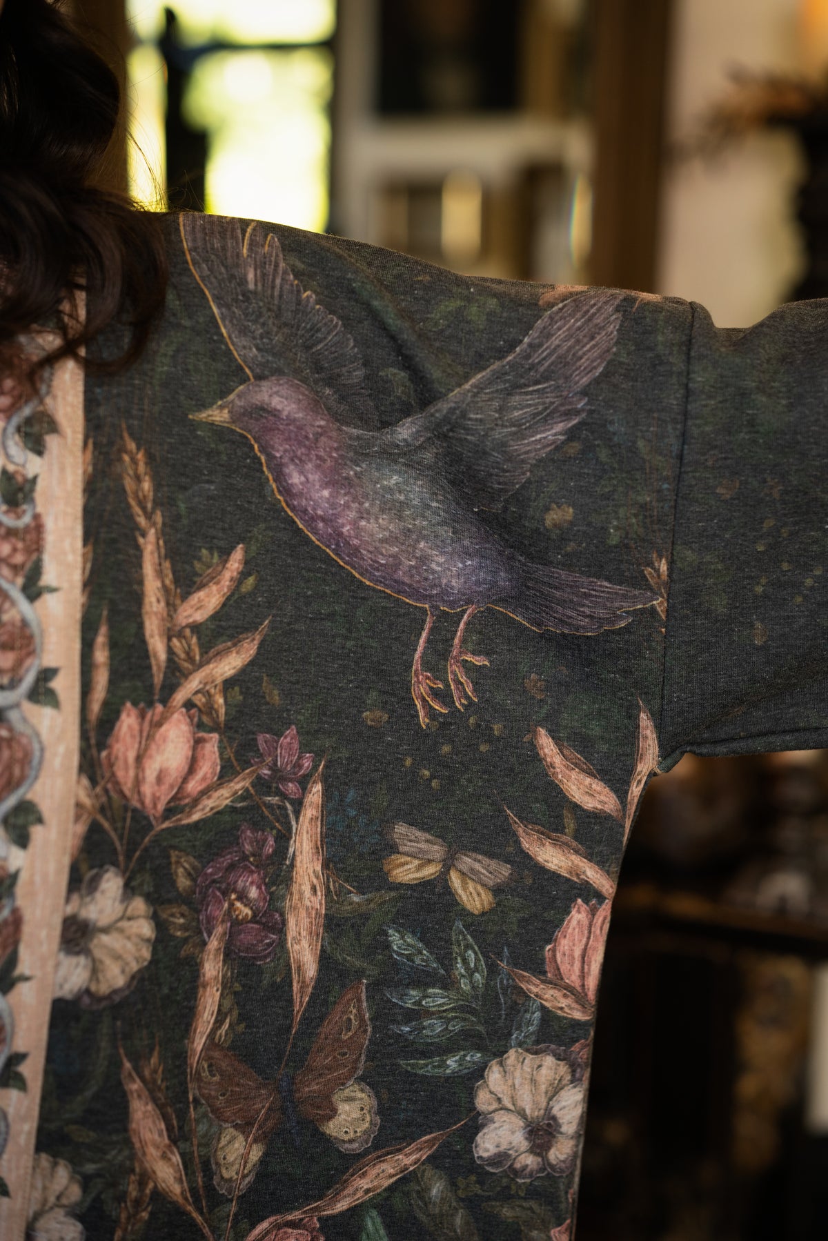 Model wearing a cozy fleece lined cottage cardigan ft. artwork created by Jessica Roux including two starlings beneath a full moon with flowers, butterflies, moths and botanical artwork - Market of Stars