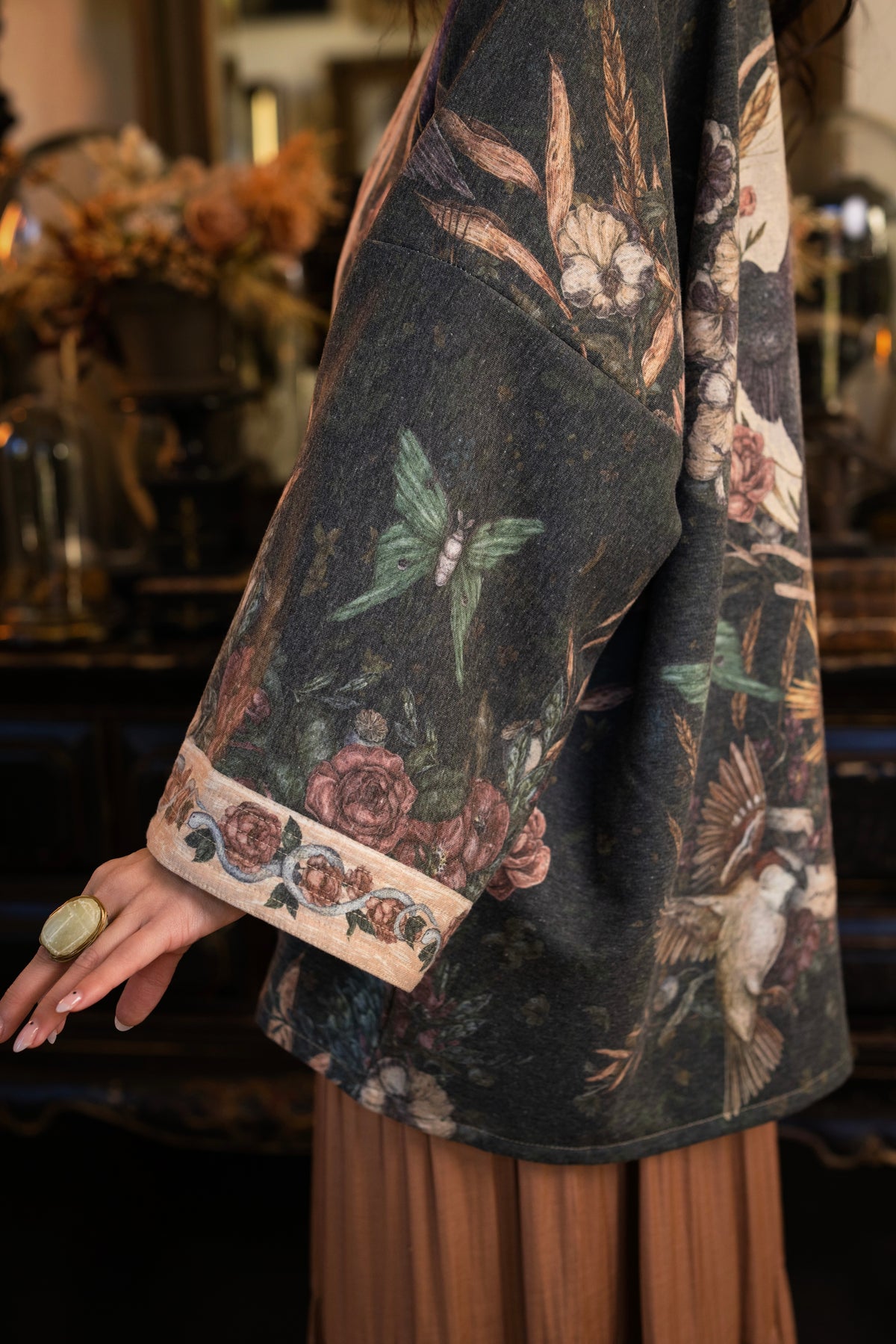 Model wearing a cozy fleece lined cottage cardigan ft. artwork created by Jessica Roux including two starlings beneath a full moon with flowers, butterflies, moths and botanical artwork - Market of Stars