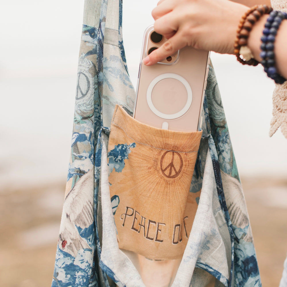 
                  
                    Model wearing our Peace Out tote bag featuring 1800's perfumeur sign with gentle tones of blue & aqua, landscapes, clouds, dove, and peace symbols -Market of Stars.
                  
                