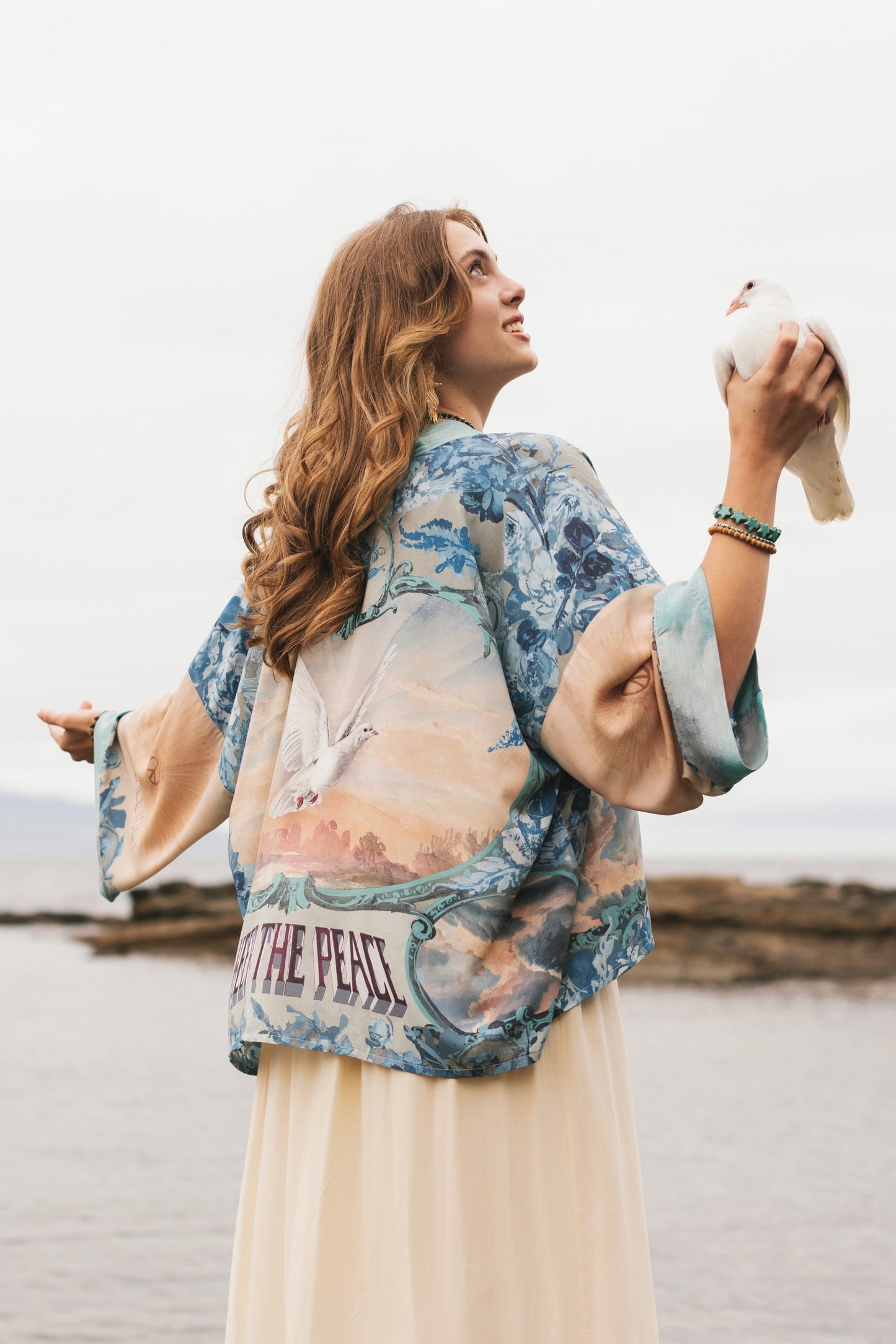 Model wearing our Peace Out Pixie Duster featuring 1800's perfumeur sign with gentle tones of blue & aqua, landscapes, clouds, dove and peace symbols -Market of Stars.