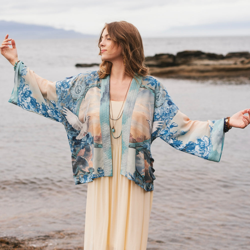 Model wearing our Peace Out Pixie Duster featuring 1800's perfumeur sign with gentle tones of blue & aqua, landscapes, clouds, dove and peace symbols -Market of Stars.