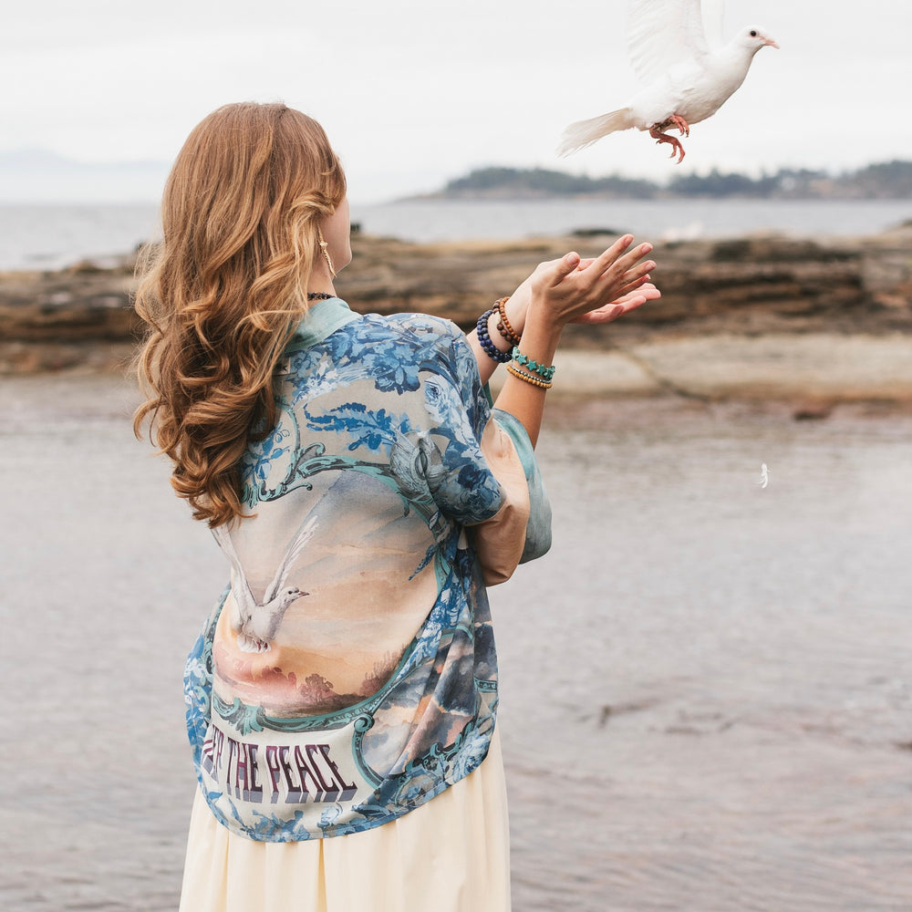 
                  
                    Model wearing our Peace Out Pixie Duster featuring 1800's perfumeur sign with gentle tones of blue & aqua, landscapes, clouds, dove and peace symbols -Market of Stars.
                  
                